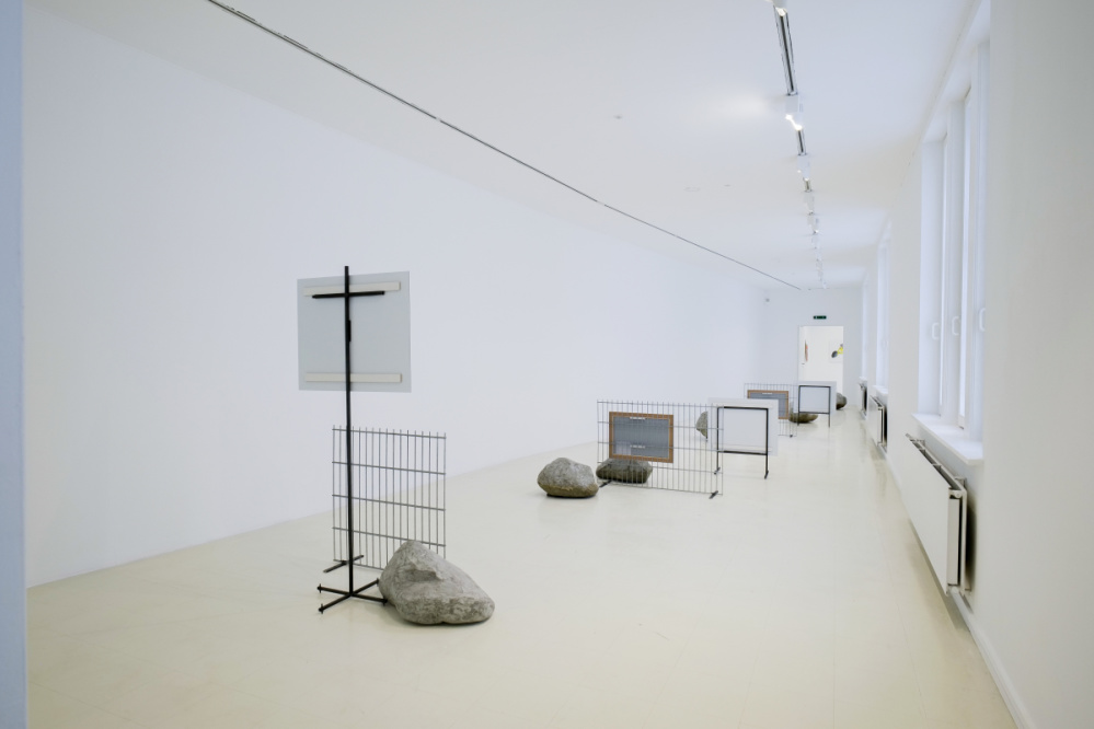 Ausstellungsansicht Natascha Sadr Haghighian "le lion malade" Blick in einen Ausstellungsraum mit Zäunen und Schildern, sowie großformatigen Steinen, die nachgebaut wurden. Die Gitterzäune sind ca. einen Meter lang und stehen im Ausstellungsraum gemeinsam mit Schildern, die von hinten gesehen werden.