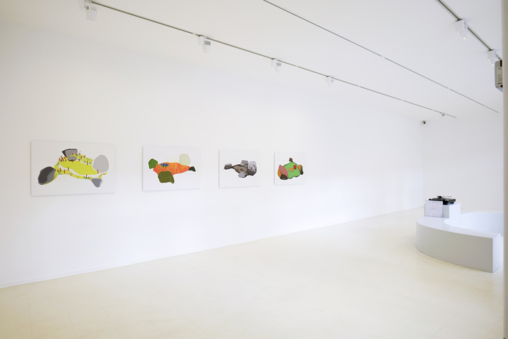 Ausstellungsansicht Natascha Sadr Haghighian "le lion malade" Blick in einen Ausstellungsraum. An der Wand Drucke im A2 Format. Rechts im Bild ein Plattenspieler mit einer gerundeten Bank zum sitzen.