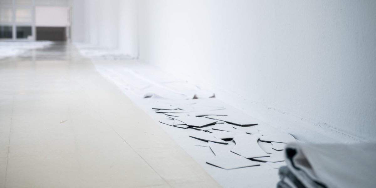 Matej Bosnić – πάσχειν (páskhein), 2021, Detail Ausstellung Stadtgalerie Blick in einen weißen Raum, der durch schwarze Kohlepulverstreifen unterteilt ist.