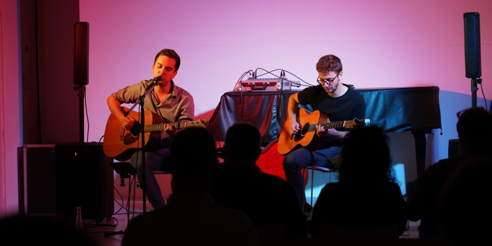 Stadtgalerie Draußen Konzert von Lukas Schüßler und Phillipp Herget Veranstaltungsraum der Stadtgalerie, Umrisse von einem Publikum, zwei männliche Gitarrenspieler auf der Bühne