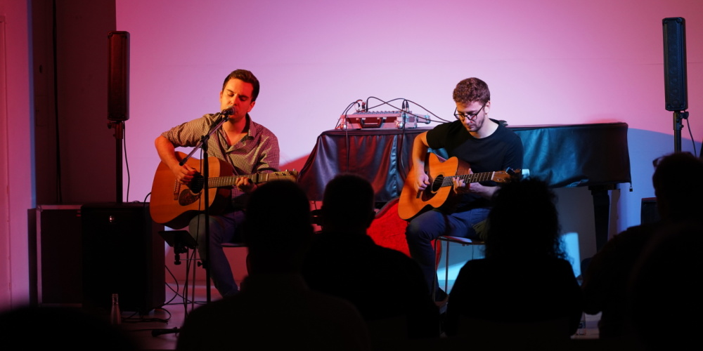 Stadtgalerie Draußen Konzert von Lukas Schüßler und Phillipp Herget Veranstaltungsraum der Stadtgalerie, Umrisse von einem Publikum, zwei männliche Gitarrenspieler auf der Bühne