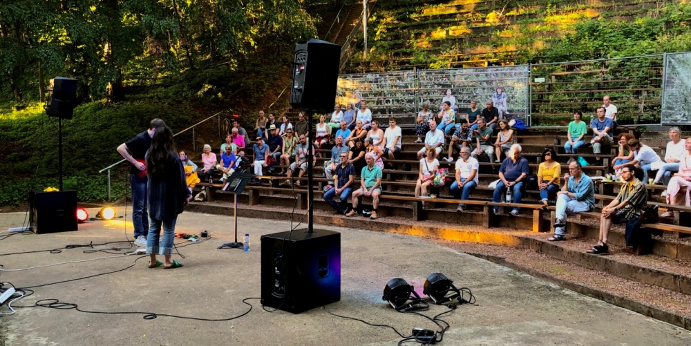Jomila und Steffen Reintgen DFG Konzert Bühne des Deutsch-Französischen Gartens, im Hintergrund sitzt das Publikum, links Sängerin und Gitarrist