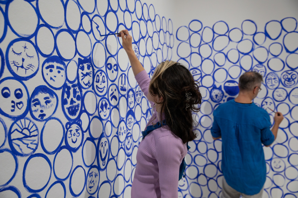 Today I feel like…Stadtgalerie, 2023 - Jeppe Hein Wand bemalt mit blauen Kreisen, zwei Menschen, die Gesichter in die blauen Kreise malen