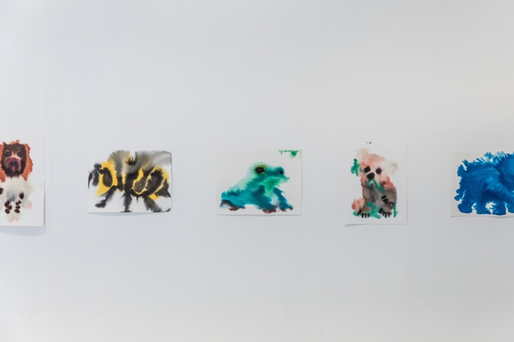 WILD ANIMALS - Rop van Mierlo Weiße Wand auf der fünf bemalte Papiere kleben, auf den Papieren sind mit Wasserfarben gemalte Tiermotive. Ein Hund, eine Biene, ein Frosch, ein Koala und ein Elefant.