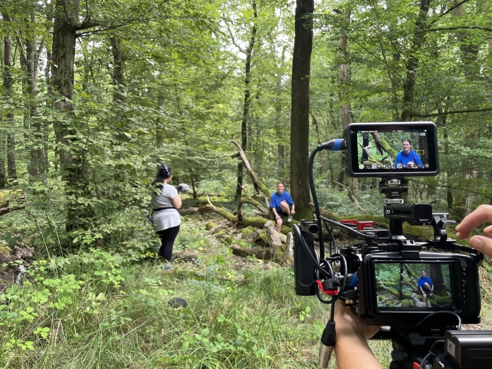 Experimental- und Kunstprojekt La Capsule, Mai - August 2024 Kamera im Vordergrund, die eine Szene in einem Wald mit einer Figur filmt