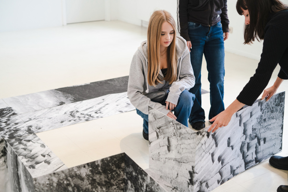 Kinder Eröffnung SUMM SUMM SUMM Stadtgalerie Eine Jugendliche beobachtet eine Person, die ein Bild faltet