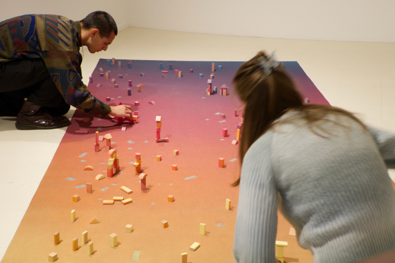 Eröffnung SUMM SUMM SUMM Stadtgalerie Zwei Personen spielen auf einem Teppich mit Holzklötzen